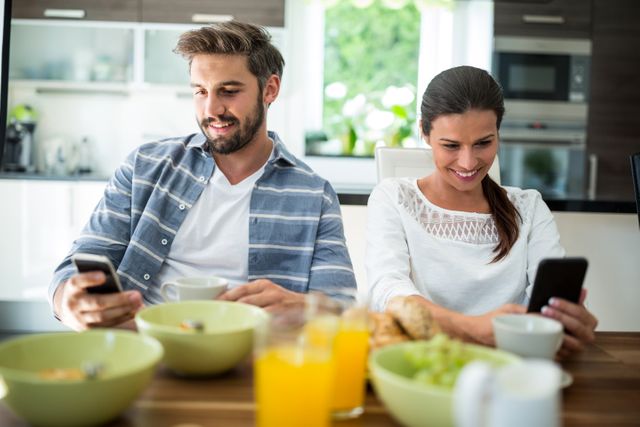 Couple using mobile phone while having breakfast at home