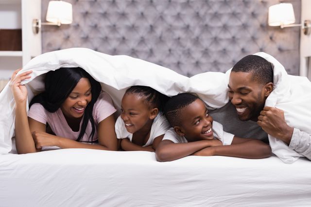 Happy family lying together under blanket on bed - Download Free Stock Photos Pikwizard.com