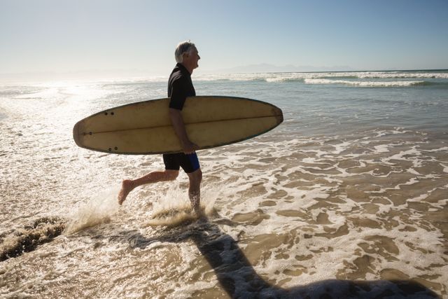 Side view of man carrying surfboard while walking on shore - Download Free Stock Photos Pikwizard.com