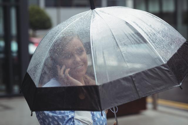 Woman holding umbrella while talking on mobile phone - Download Free Stock Photos Pikwizard.com