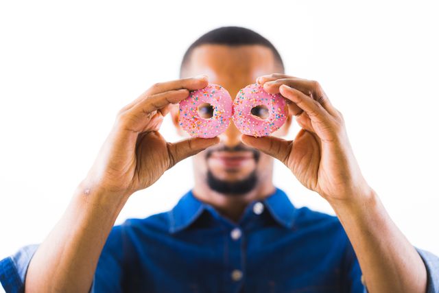 African american man holding pink donuts in front of face against white background - Download Free Stock Photos Pikwizard.com