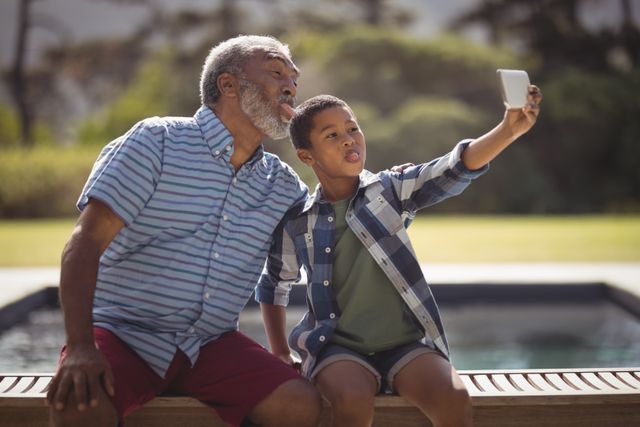 Grandson and grandfather taking selfie with mobile phone near poolside