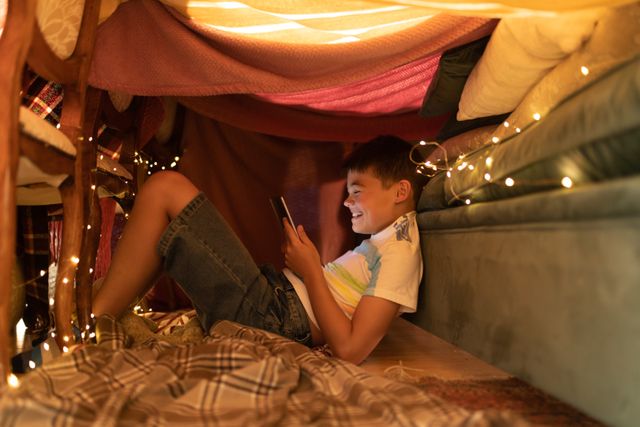Side view of a caucasian boy sitting on the floor leaning on the couch inside his blanket fort while - Download Free Stock Photos Pikwizard.com