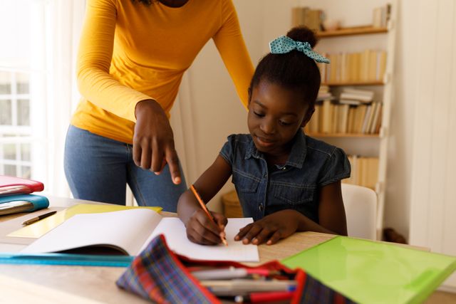 Font view of an african-american girl writing notes with her mother standing beside her helping her  - Download Free Stock Photos Pikwizard.com