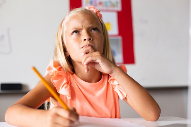 Thoughtful caucasian elementary girl with hand on chin thinking while writing on book - Download Free Stock Photos Pikwizard.com