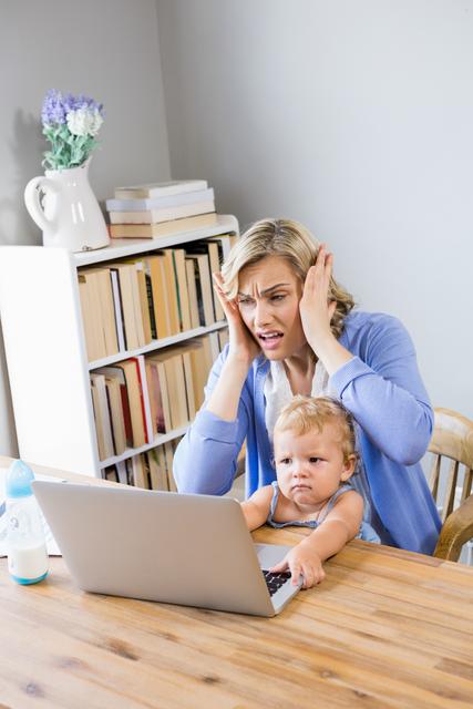 Stressed mother with baby girl using laptop at home