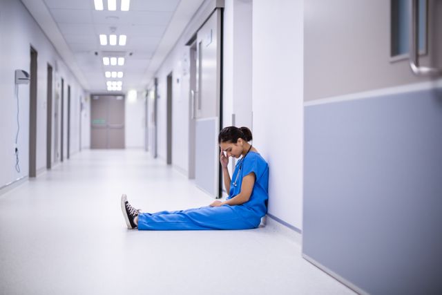 Tensed female doctor sitting in corridor - Download Free Stock Photos Pikwizard.com