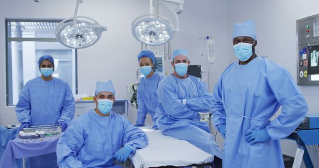 Diverse male and female doctors wearing face masks standing in operating theatre smiling to camera. medicine, health and healthcare services during coronavirus covid 19 pandemic.