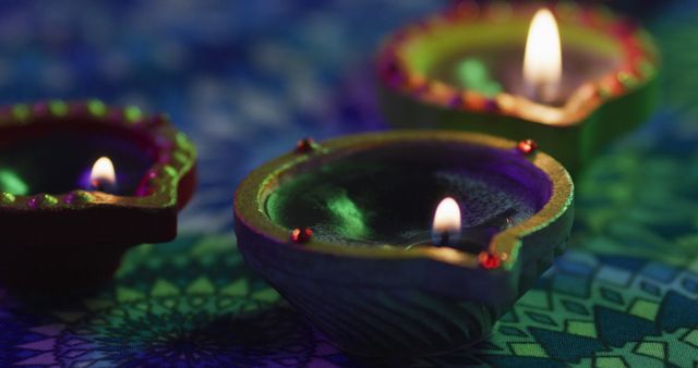 Lit candles in decorative clay pots on patterned table top, focus on foreground, bokeh background. diwali festival, celebration, tradition and ceremony concept.