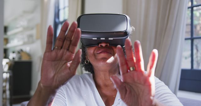 Senior african american woman sitting on sofa and using vr headset. Senior lifestyle, free time, communication and domestic life.