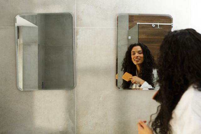 Mixed race woman standing in bathroom brushing her hair and smiling - Download Free Stock Photos Pikwizard.com