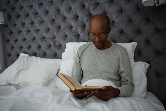Senior man reading book while sitting on bed - Download Free Stock Photos Pikwizard.com