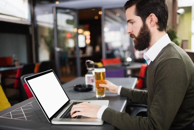 Man using laptop while having glass of beer in bar