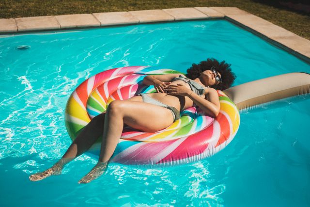 Mixed race woman lying on inflatable toy in the pool sunbathing and relaxing - Download Free Stock Photos Pikwizard.com