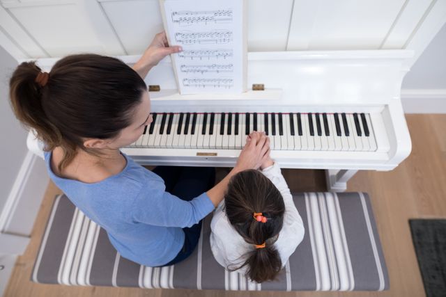Overhead of mother assisting daughter in playing piano - Download Free Stock Photos Pikwizard.com