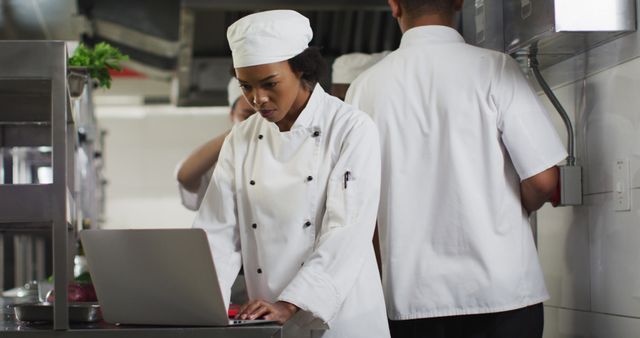 African american female chef using laptop in restaurant kitchen. Working in a busy restaurant kitchen.