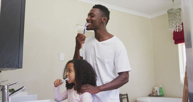 Happy african american father and daughter brushing teeth together in bathroom at home. Fatherhood, childhood, domestic life and self care.