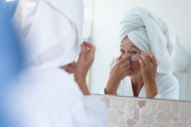 Mature caucasian woman using under eye treatment patch looking in bathroom mirror, copy space - Download Free Stock Photos Pikwizard.com