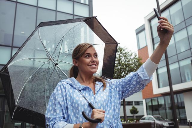 Beautiful woman holding umbrella while taking selfie - Download Free Stock Photos Pikwizard.com
