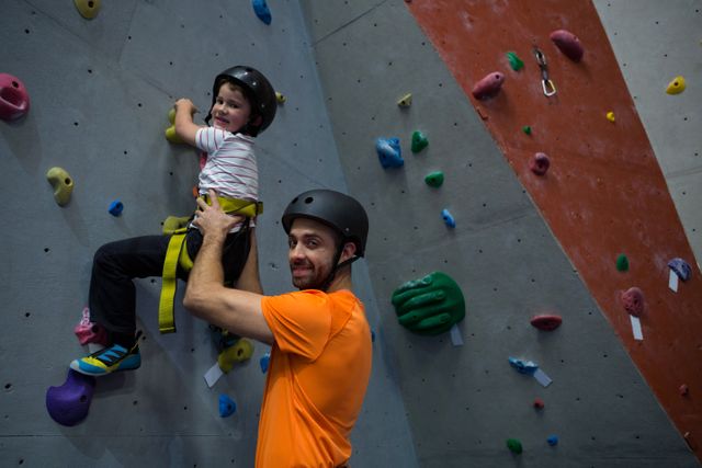 Trainer assisting boy in rock climbing at fitness studio