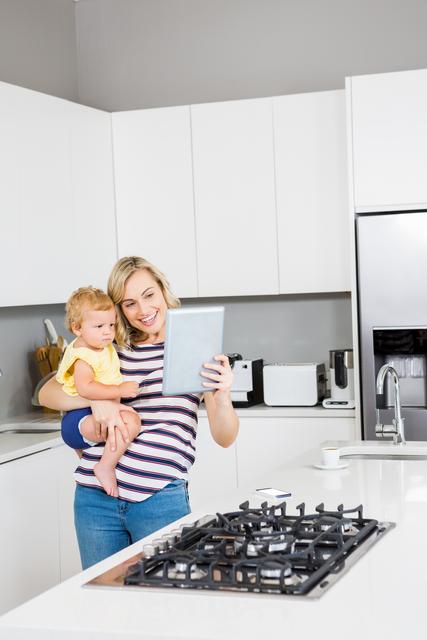 Mother and baby girl using digital tablet in kitchen - Download Free Stock Photos Pikwizard.com