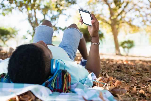 Young man using mobile phone while lying on a picnic blanket - Download Free Stock Photos Pikwizard.com