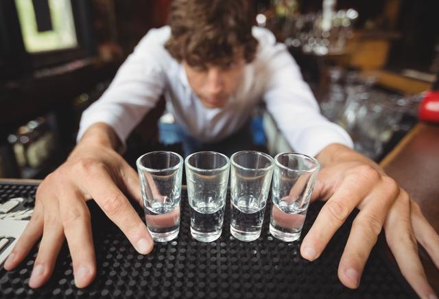 Bartender preparing and lining shot glasses for alcoholic drinks on bar counter at bar