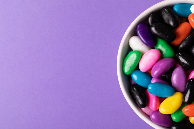 Directly above view of colorful candies in bowl by copy space on purple background. unaltered, sweet food, unhealthy eating concept.