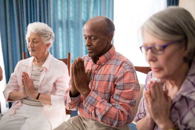 Senior man amidst women praying while sitting on chairs - Download Free Stock Photos Pikwizard.com