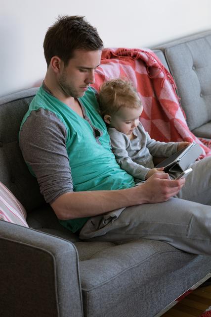 Man showing tablet computer to daugher while sitting on sofa at home