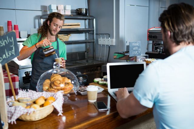 Customer using laptop at counter while staff preparing coffee - Download Free Stock Photos Pikwizard.com