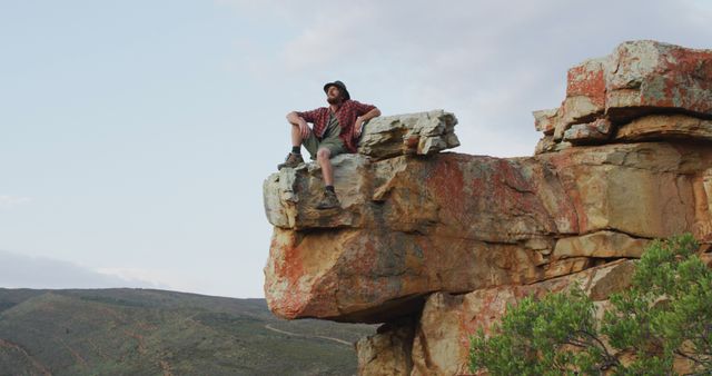 Happy caucasian male survivalist sitting on rocky mountain peak in wilderness, enjoying the view. exploration, travel and adventure, survivalist in nature.