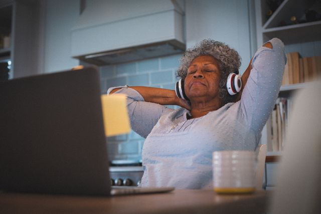 Happy african american senior woman wearing headphones relaxing in kitchen with eyes closed - Download Free Stock Photos Pikwizard.com