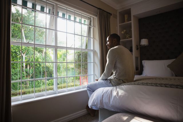 Man sitting on bed by window in bedroom - Download Free Stock Photos Pikwizard.com