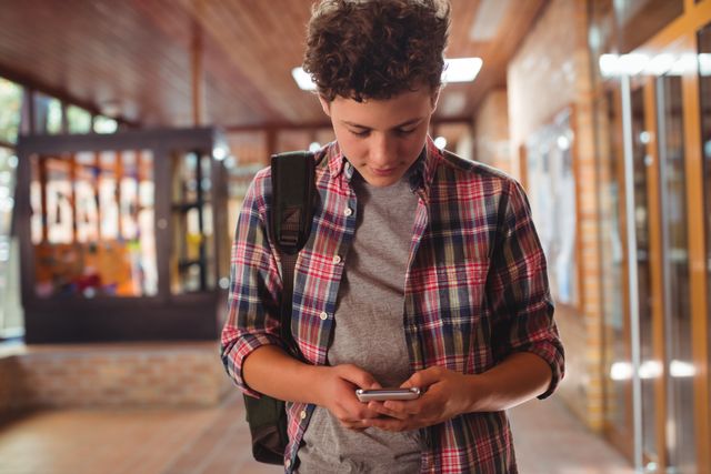 Schoolboy using mobile phone in corridor at school - Download Free Stock Photos Pikwizard.com