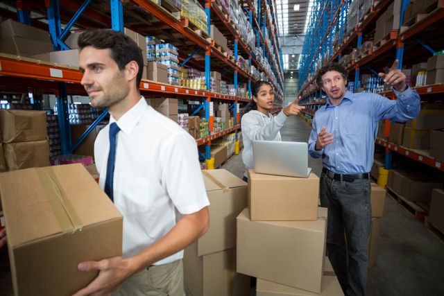Warehouse manager carrying a box and his colleagues discussing - Download Free Stock Photos Pikwizard.com