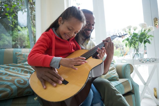 Father and daughter playing guitar together in living room - Download Free Stock Photos Pikwizard.com