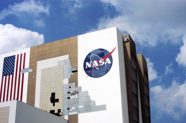 KENNEDY SPACE CENTER, FLA. -  On a scaffold barely visible along the south wall of the Vehicle Assembly Building near the NASA logo, workers are covering the holes with corrugated steel so the facility can be returned to performing operational activities. The VAB lost 820 panels from the south wall during the storm, and 25 additional panels pulled off the east wall by Hurricane Jeanne.  Another scaffold is suspended near the top of the east wall (right side) for repairs.  The VAB stands 525 feet tall.  Central Florida, including Kennedy Space Center, has been battered by four hurricanes between Aug. 13 and Sept. 26.