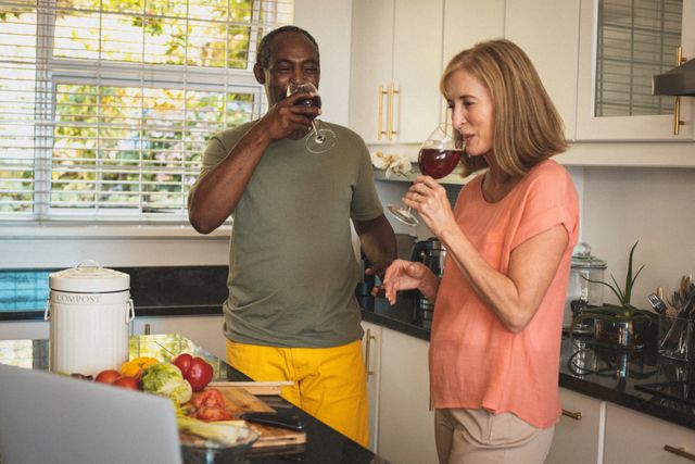Diverse senior couple drinking red wine in the kitchen - Download Free Stock Photos Pikwizard.com
