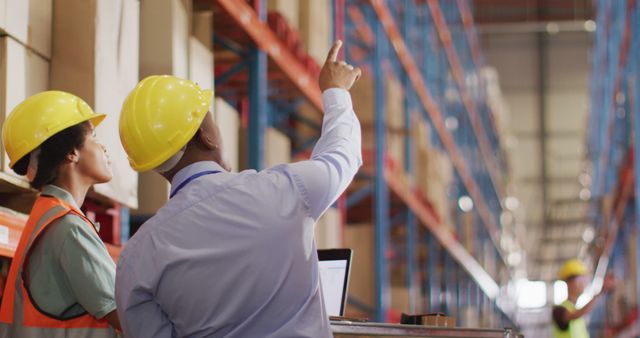 African american male and female workers wearing helmet and using laptop in warehouse. global business, shipping and delivery.