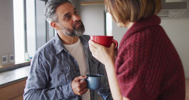 Happy diverse couple in kitchen together drinking coffee and talking. Spending quality time at home.