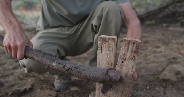 Caucasian male survivalist using branch and machete to cleave firewood at camp in wilderness. exploration, travel and adventure, survivalist in nature.