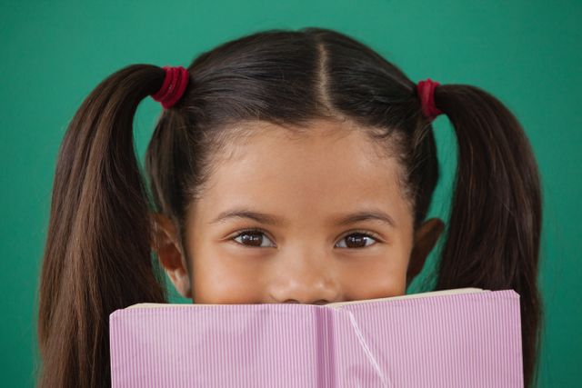 Schoolgirl hiding behind a book against green background - Download Free Stock Photos Pikwizard.com