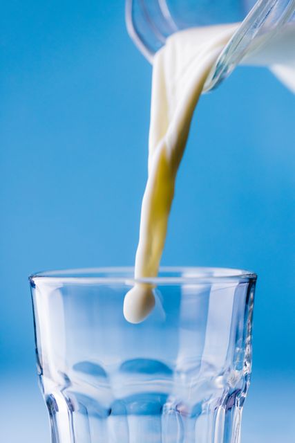 Close-up of milk being poured in jug against blue background, copy space - Download Free Stock Photos Pikwizard.com