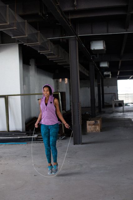 African american woman wearing sports clothes skipping the rope in empty urban building. urban fitness healthy lifetyle.