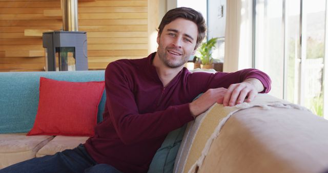 Image of happy caucasian man sitting on sofa and looking at camera. Lifestyle and spending time at home concept.