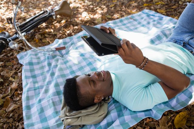 Man using digital while lying on a picnic blanket - Download Free Stock Photos Pikwizard.com