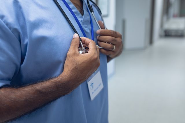 Mid section of mixed race male doctor standing with stethoscope in the corridor at hospital