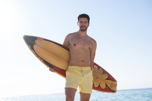 Young shirtless man holding surfboard at beach on sunny day - Download Free Stock Photos Pikwizard.com