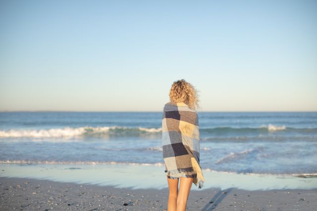 Woman wrapped in blanket standing on the beach - Download Free Stock Photos Pikwizard.com